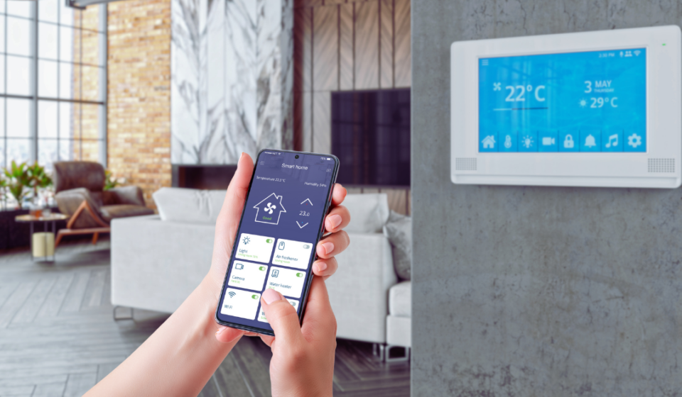 A person holding a smartphone displaying their IAQ monitoring system, connected to a smart thermostat for real-time indoor air quality control.